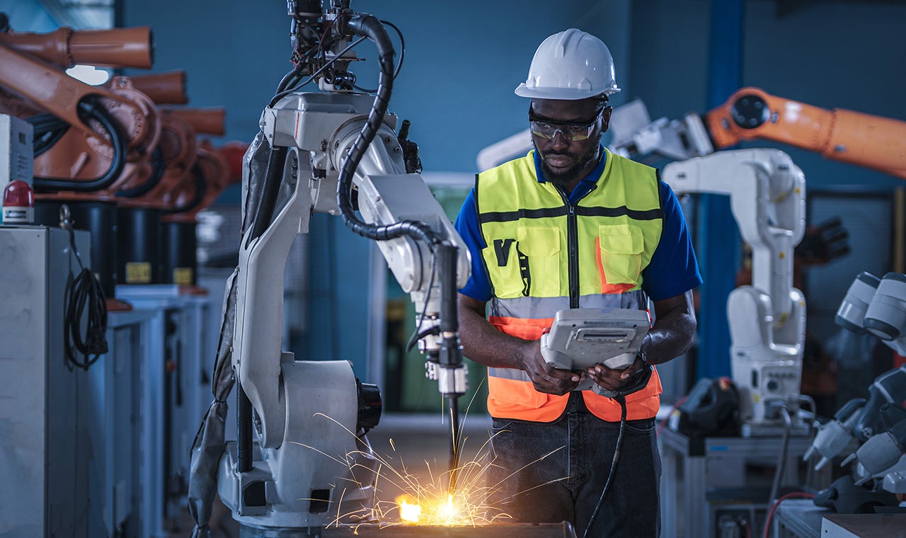 Engineers in safety equipment controlling a welding robotic arm