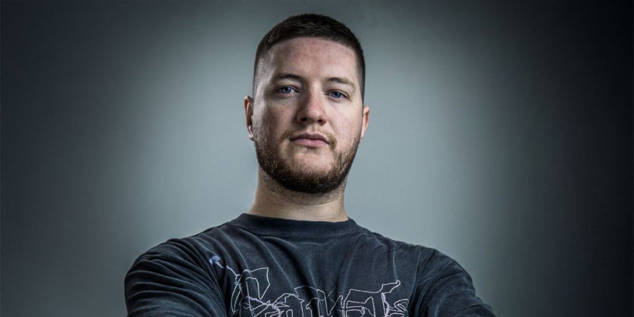 Person wearing a dark graphic T-shirt is standing with arms crossed against a neutral gray background, creating a strong and confident pose.