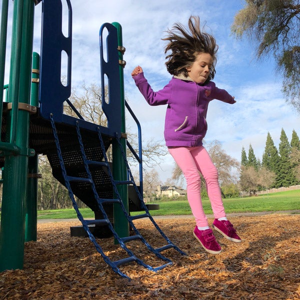 A dynamic image of a girl jumping from a jungle gym