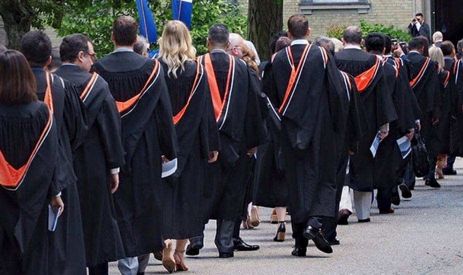Graduation ceremony. Line of graduates walking towards building.