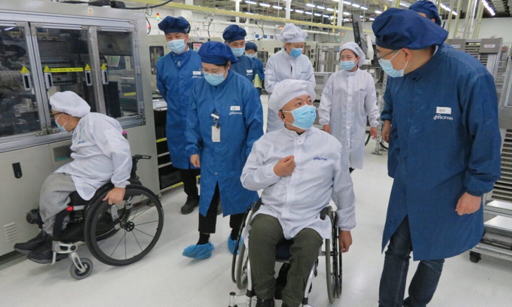 Workers in protective clothing move through an industrial facility, with some using wheelchairs.