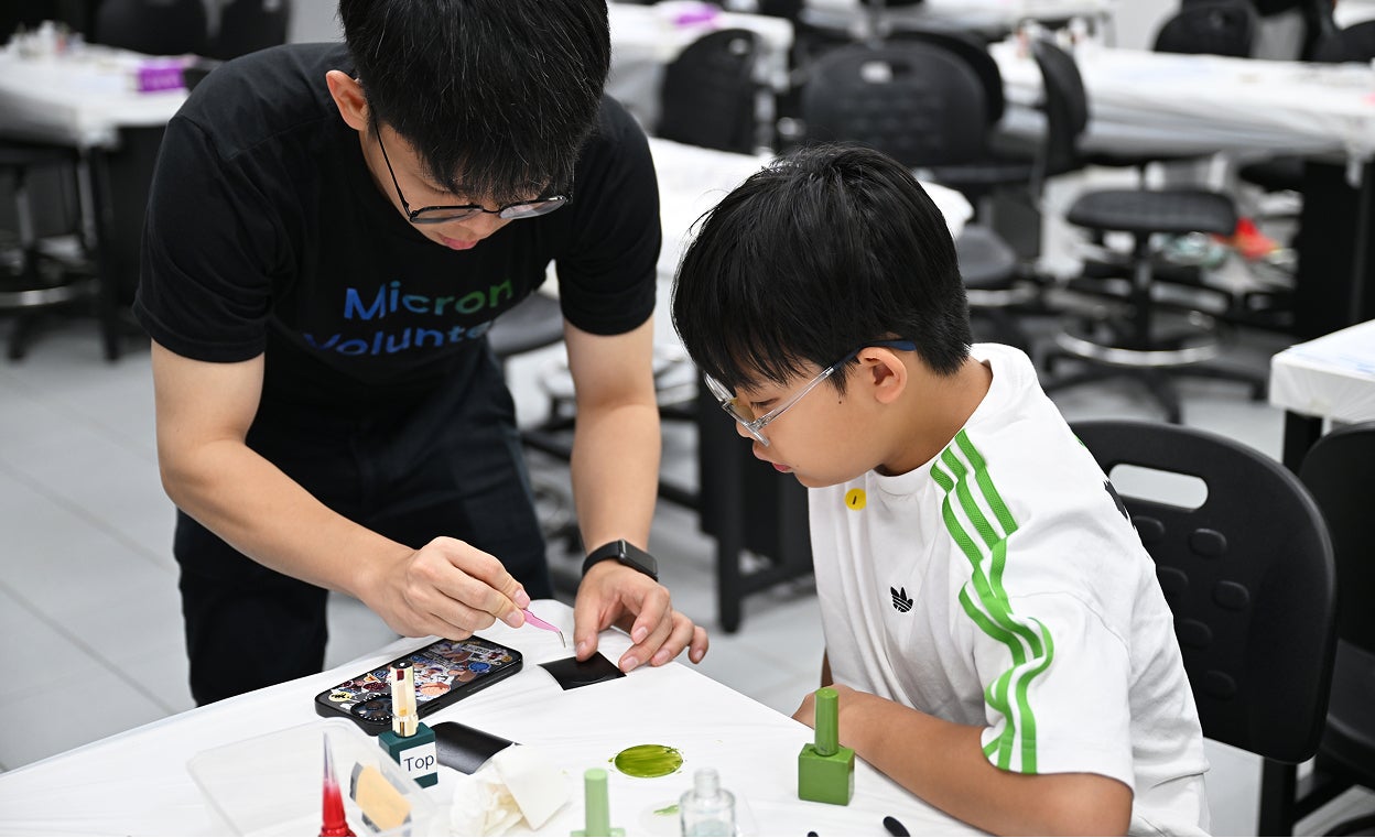 Micron volunteer assisting a student with a hands-on STEM activity.