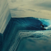 Surfer riding a wave toward a surreal ocean edge that appears to drop into space