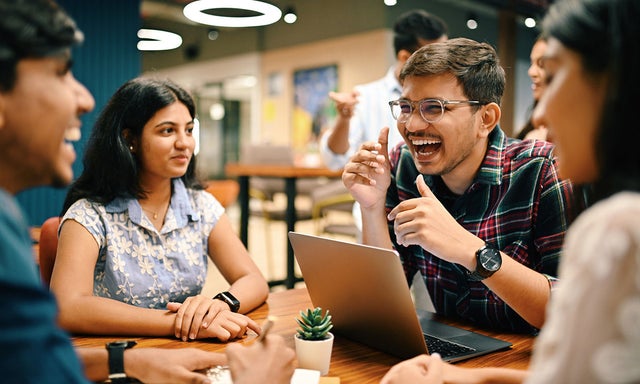 Group of students laughing at a table with a laptop in front of one of them.