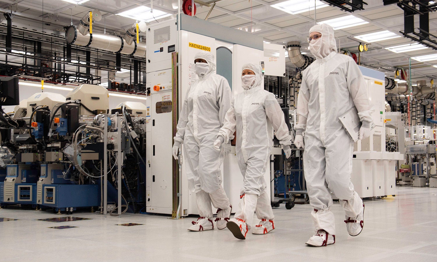 Three fabrication plant workers walking through clean room