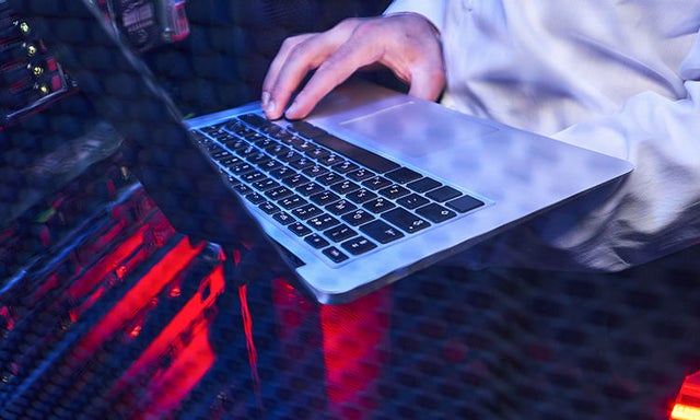 A laptop on a clear desk with red underlighting and a hand touching the keyboard.