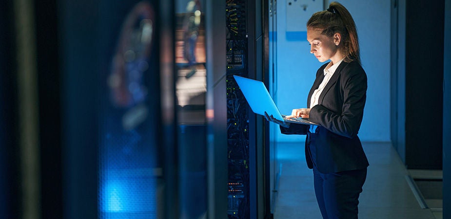 A woman standing in a data center working on a laptop 