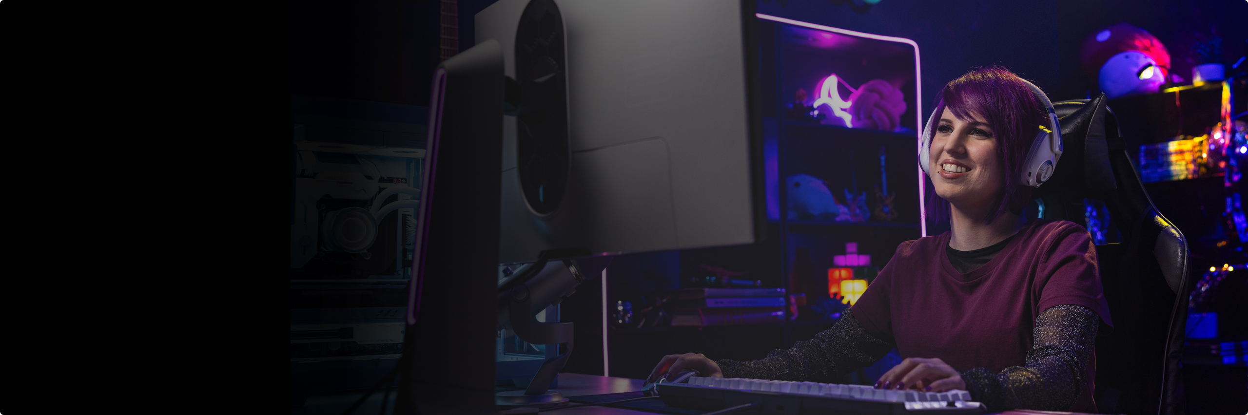 Girl with purple hair and headphones playing on a PC and smiling in a darker, decorated room with purple and blue LED lighting.