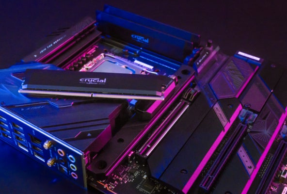 Placa base bajo luz rosa y azul en superficie oscura con Crucial DDR5 Pro instalada y visualizada.