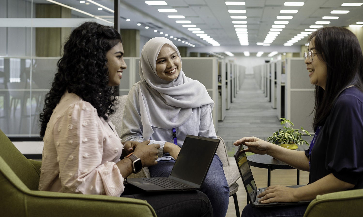 Three women sitting, smiling, and talking to each other in office