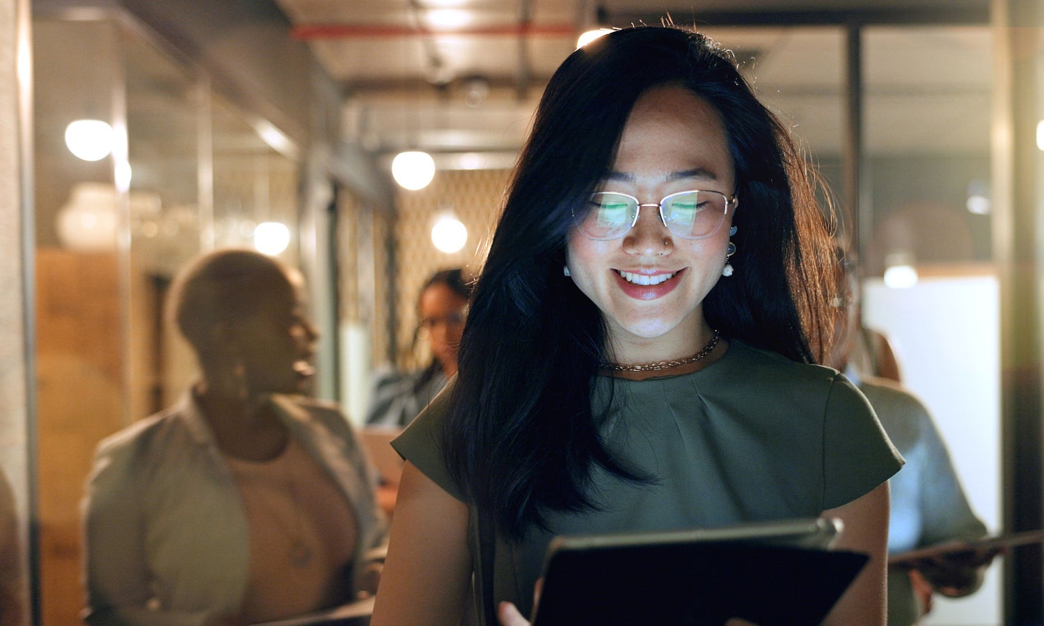 Smiling woman standing in office hallway reading a tablet