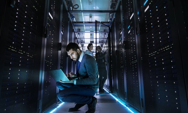 A dark data center with a technician at a server rack with a laptop