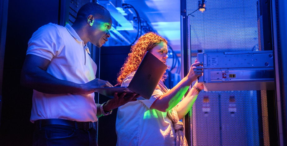 Person standing in front of an open shelf in data center with laptop in one hand
