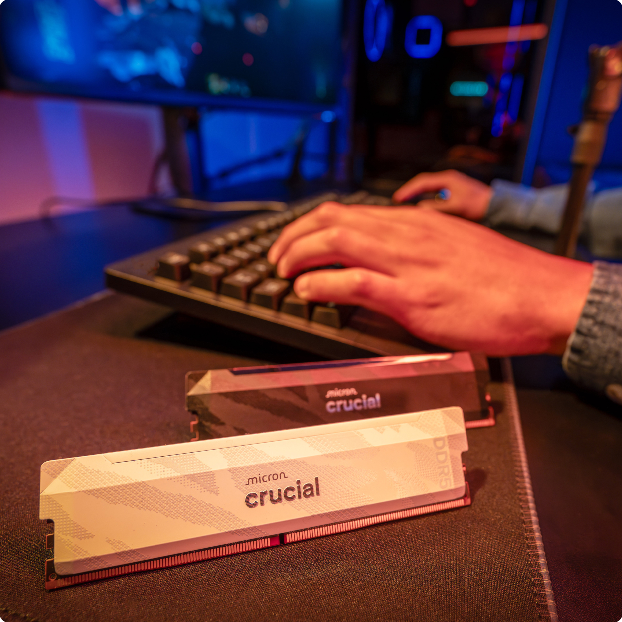 Close shot of two white Crucial Pro DDR5-6400 modules on a glass top desk next to a woman's hand using a keyboard.
