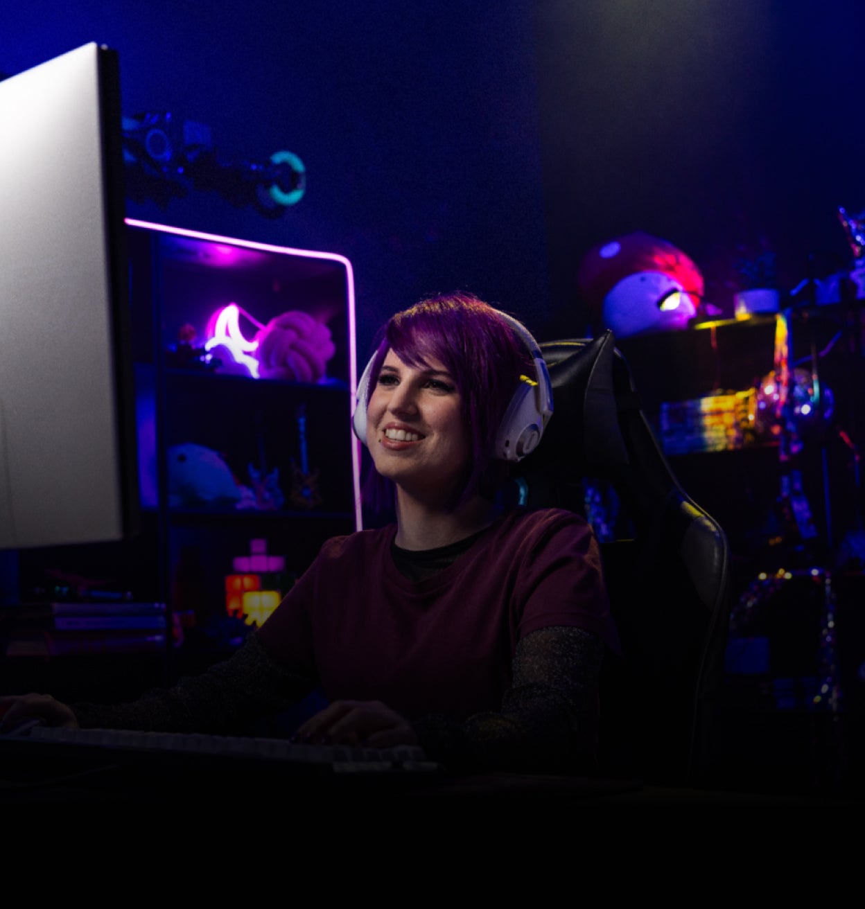  Una donna sorridente con le cuffie, seduta, che gioca su un PC da gioco.