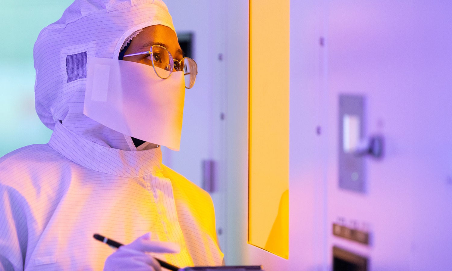 Woman recording notes in lab wearing a cleanroom suit