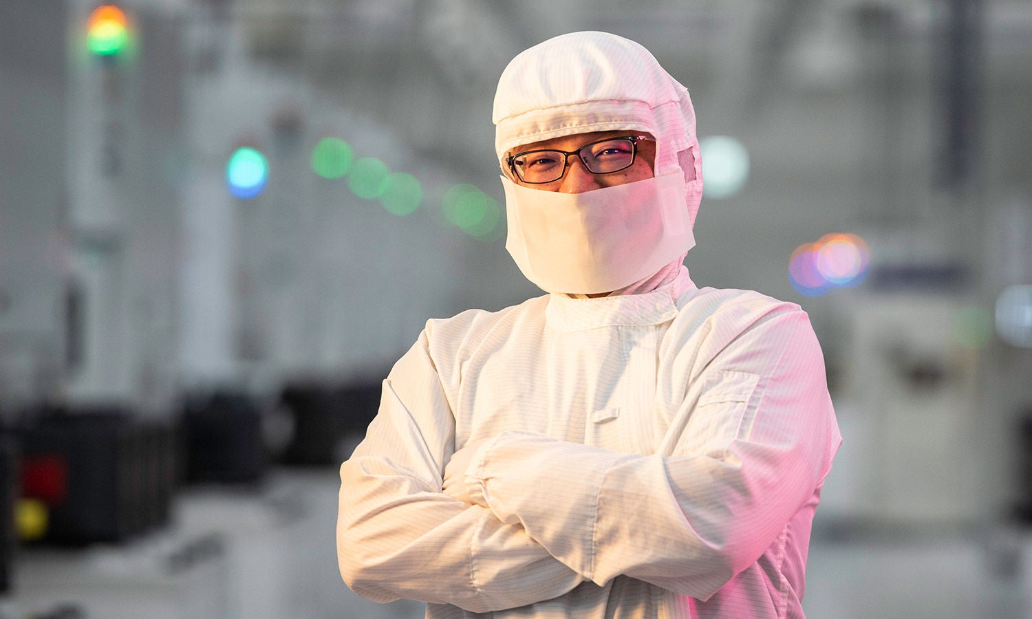 Person in full cleanroom suit with arms crossed in a semiconductor facility.