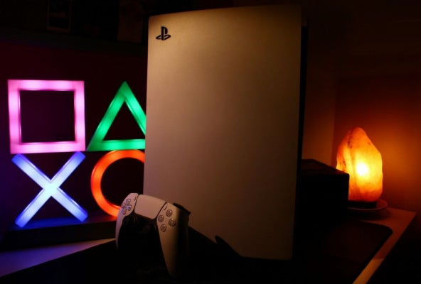 PlayStation 5 console and controller displayed in dark room with the PlayStation symbols in background.