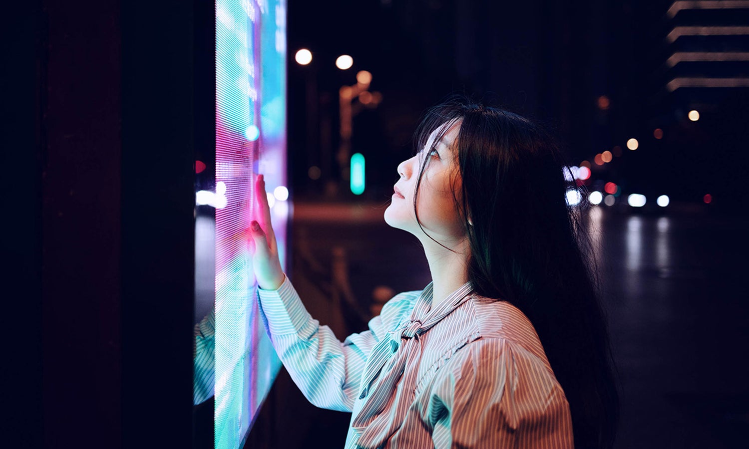 Woman interacting with a public touch screen, at night.