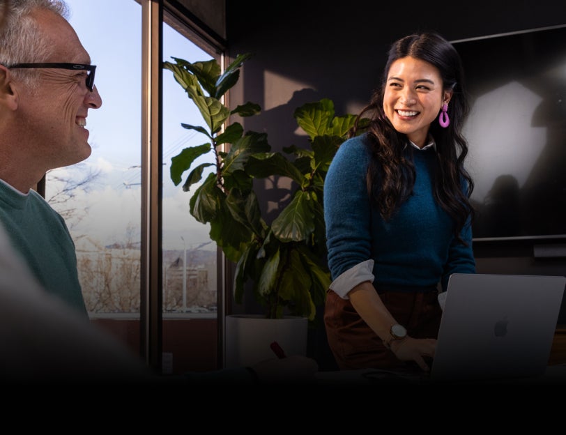  A woman sitting on a balcony overlooking a forest and working on a laptop.