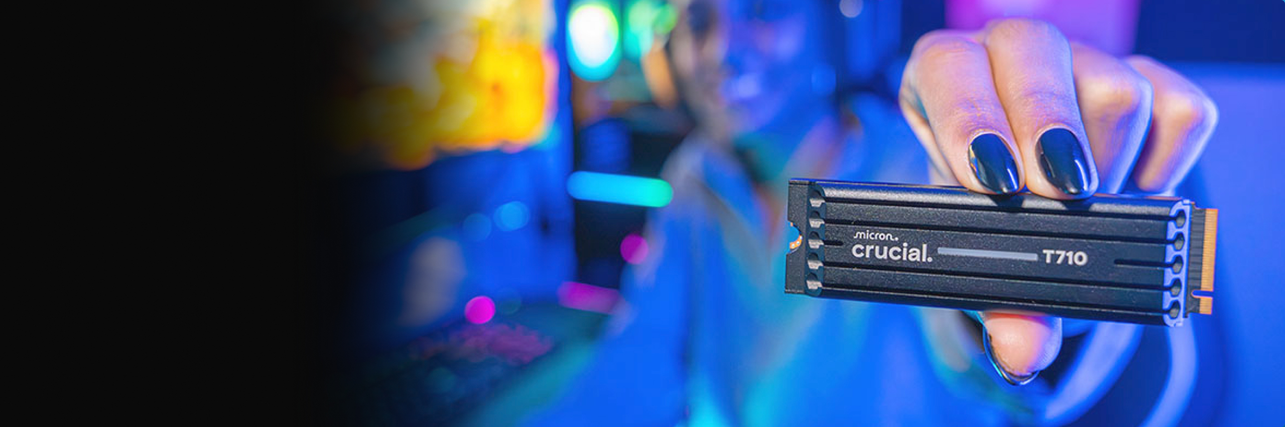 A hand installing a Crucial T705 NVMe M.2 SSD into the motherboard slot of a gaming desktop PC with the side cover removed and other internals visible.