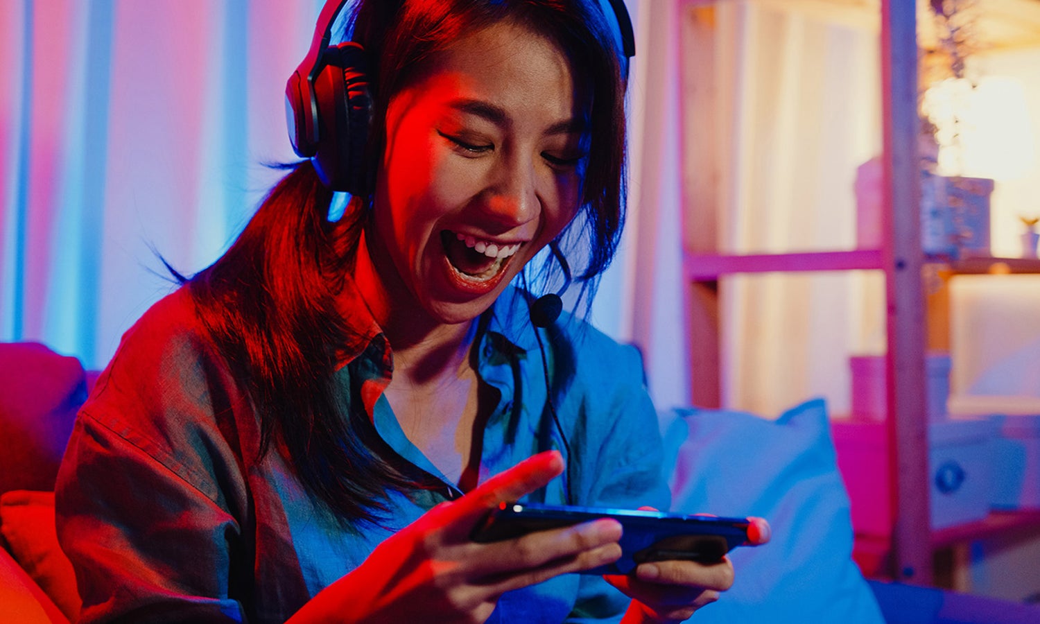 Female wearing headphones and looking down excitedly at a device she is holding