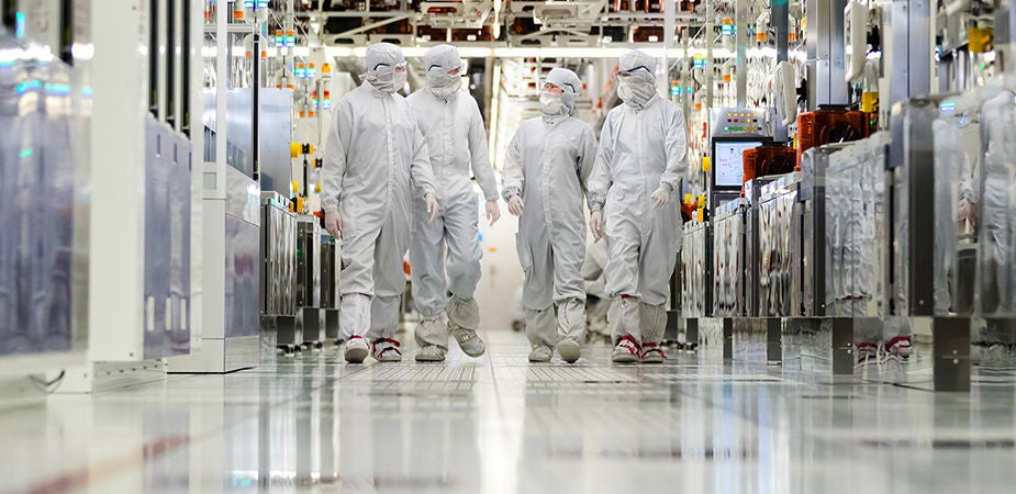 Fabrication plant workers in clean suits walking down a hallway