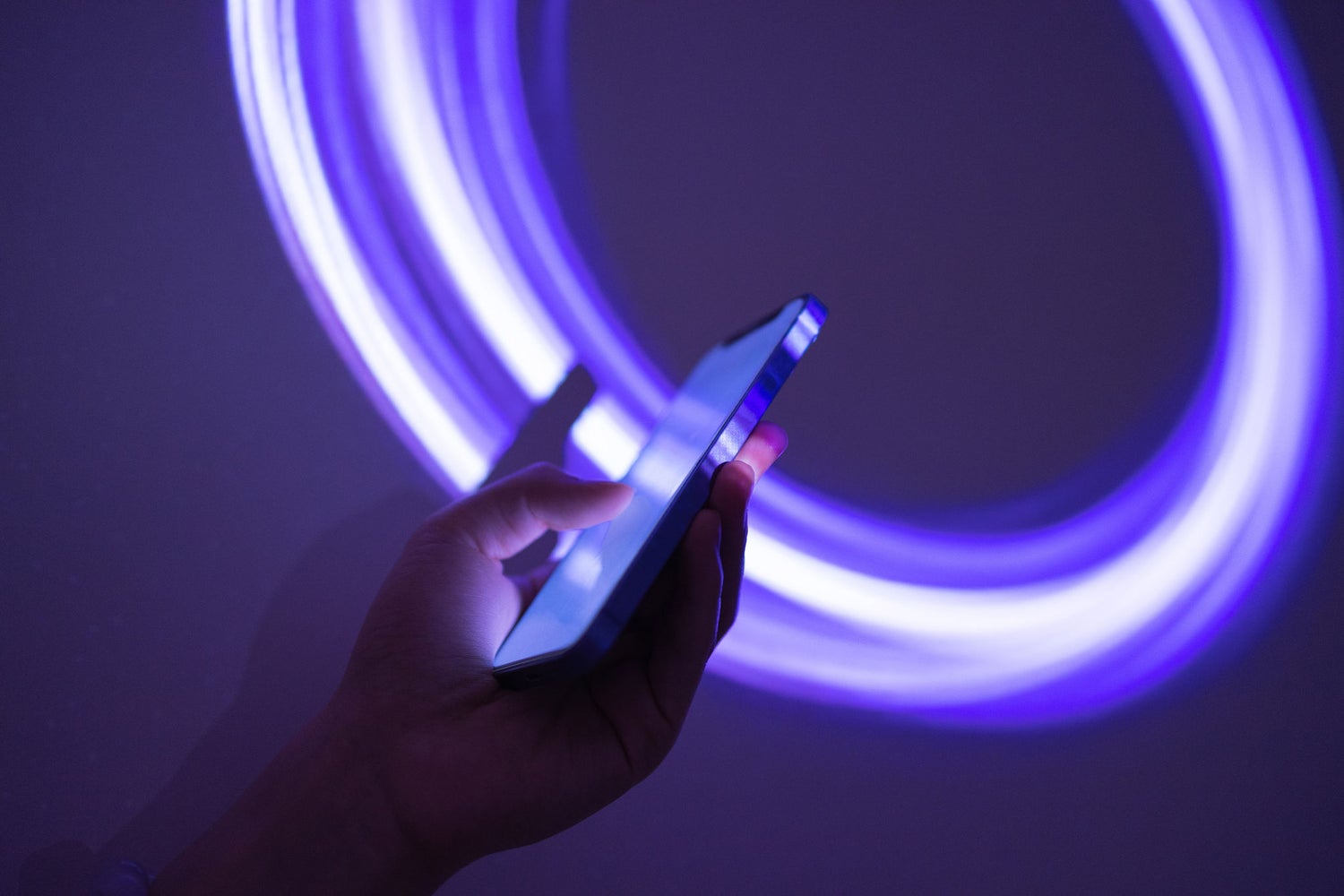 Hand holding mobile device with a glowing purple circle in the background