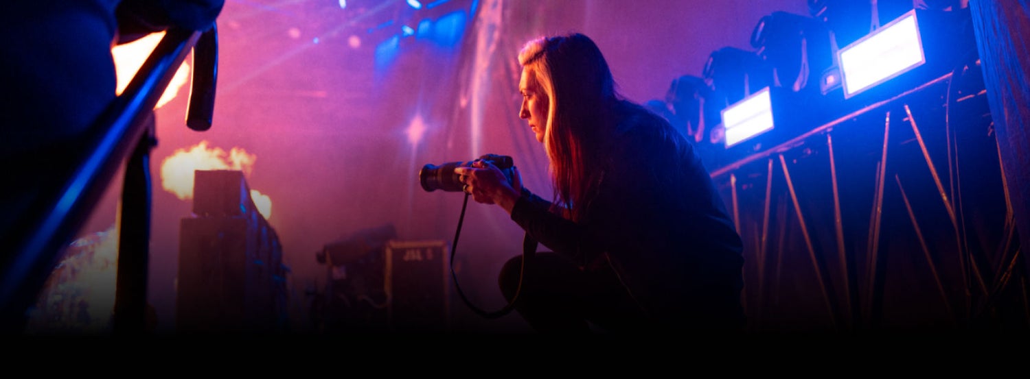 A photographer is crouched down backstage behind a concert getting ready to take a photo.
