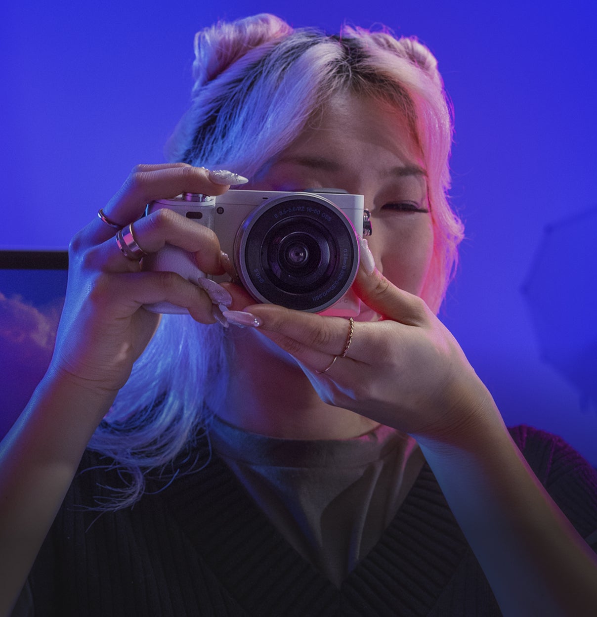 カメラを顔に向けて写真を撮ろうと構える、デニムジャケットの人物。青と紫の照明に照らされた背景が、スタジオのような生き生きとした雰囲気を演出している。