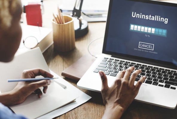 Person sitting at desk on a laptop writing and waiting for a program to finish uninstalling.