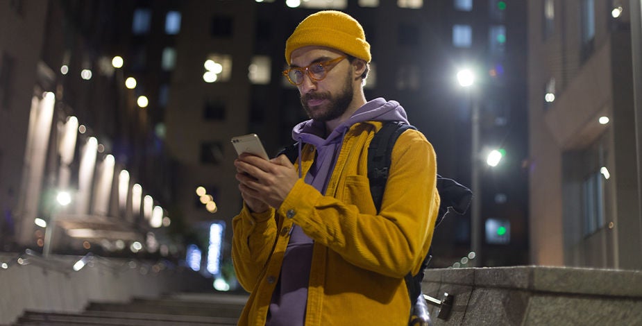 A man looking at his mobile phone on a city street at night.