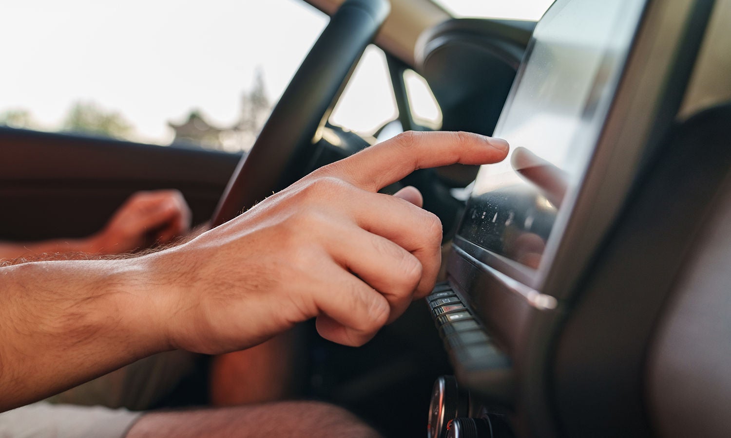 A driver in a parked car using their automobile's touchscreen.