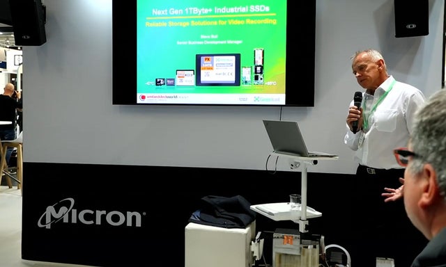 Man presenting with a microphone and a green monitor in the background